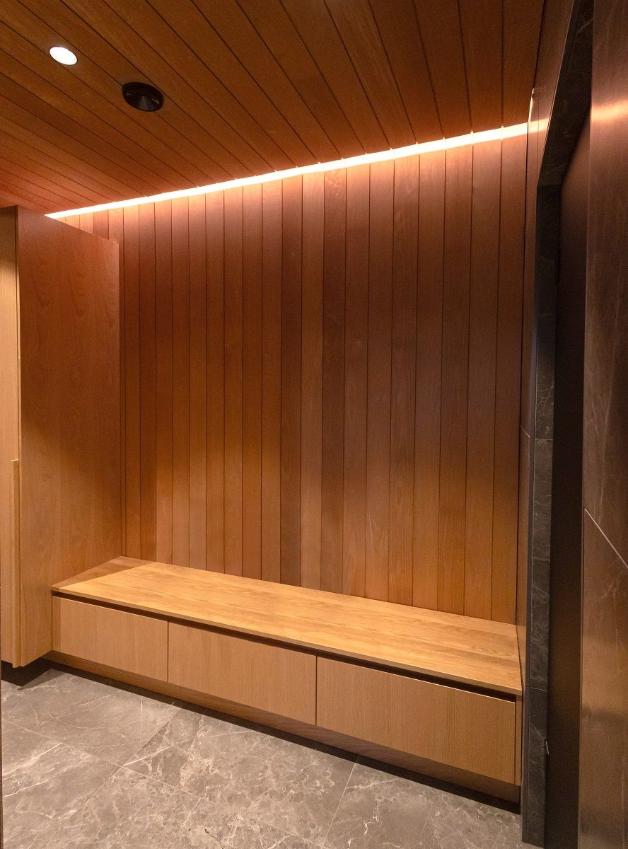 Una striscia di luce calda da 3 000 Kelvin in una scanalatura da soffitto a parete in uno spogliatoio rivestito in legno.